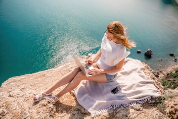 Freelance woman working on a laptop by the sea, typing away on the keyboard while enjoying the beautiful view, highlighting the idea of remote work.