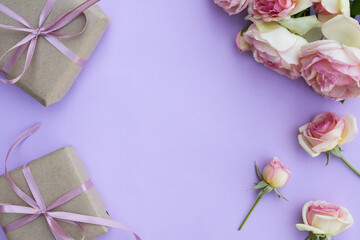 Floral frame with rose flowers, petals and gift boxes on a purple background. Flat lay, top view, copy space. Valentines day background.
