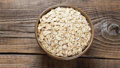 Oat flakes in a round bowl on the old wooden background, top view