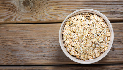 Oat flakes in a round bowl on the old wooden background, top view