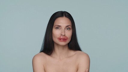 Obraz premium Brunette woman performs lip skin care procedures. Woman with hydrogel red patches on her lips in the studio on a blue background close up. Healing of dry and chapped lips, hydration.