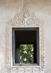 Old wooden windows with stucco frames decorated with Garuda patterns in the ubosot of the temple.