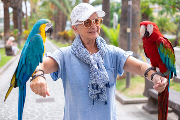 Portrait of mature elderly woman with two domestic ara parrots in the park © luciano