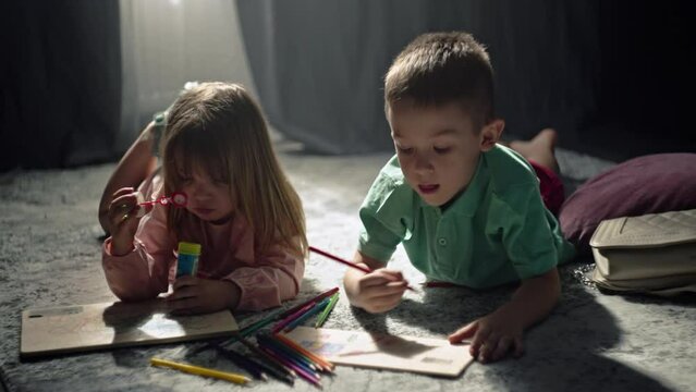 Brother and sister draw with pencils at home on the floor. A child's time spent with benefit, a happy childhood, the art of drawing. High quality 4k footage