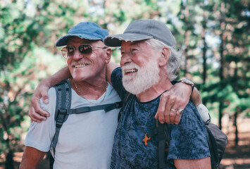 Happy couple of old active men with hat and backpack embrace and have fun in mountain hike in the...