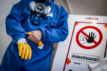 Mann säubert Gebäude von Asbest im blauen Schutzanzug mit gelben Handschuhen und einer Schutzmaske  - obrazy, fototapety, plakaty
