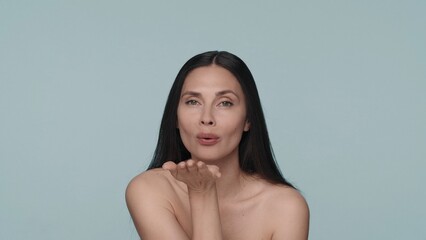 Obraz premium The woman sends an air kiss. Seminude brunette woman isolated on blue background. The concept of beauty, cosmetology, skin care.