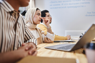 Side view portrait of Arabian business people sitting at table in row during meeting or seminar, focus on woman wearing headscarf, copy space