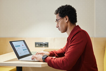 Minimal side view portrait of young Arabian businessman wearing glasses and using computer at office workplace, copy space