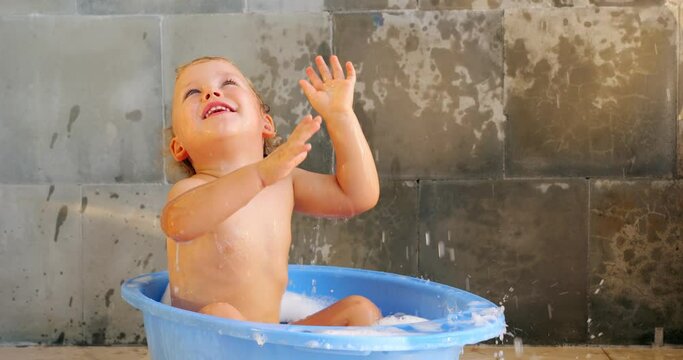 Playful and ecstatically delighted baby boy splashes around in warm baby bathtub. With joyful expressions, he tosses water, wipes his face, and continues his fun game. lively and exuberant toddler