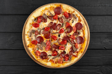 Top view of pizza with pepperoni sausages, beef, tomatoes and cheese on black wooden background