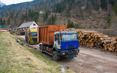 A flatbed truck loaded with timber and a container truck at a saw mill yard near the village of Forni Avoltri in Carnia, Udine Province, Friuli-Venezia Giulia, north east Italy
