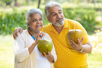 Indian senior couple drinking coconut water at park.