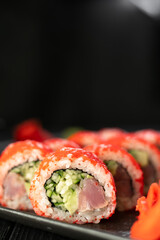 Delicious sushi roll california with tuna cucumber cheese and masago caviar on top on a stone plate on black background. Vertical banner.
