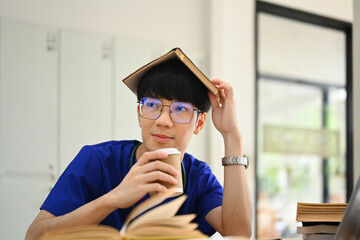 Medical student man wearing blue scrubs putting book on head and looking away. Medical internship...