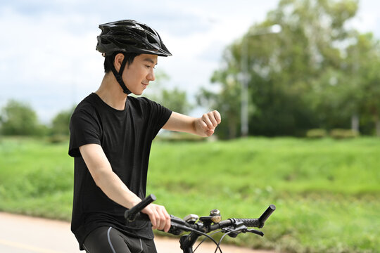 Satisfied man cyclist taking break from riding bicycle and checking sport activity progress data on smartwatch