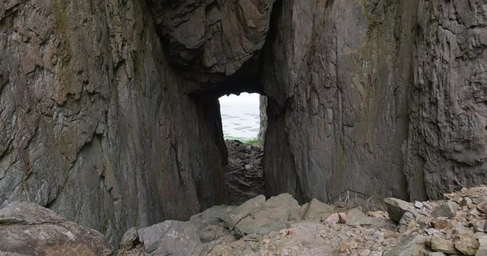 Drone reveal woman in vivid clothes by large hole through Torghatten mountain