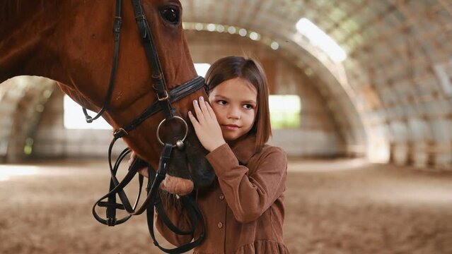 Cute little girl is with horse indoors.