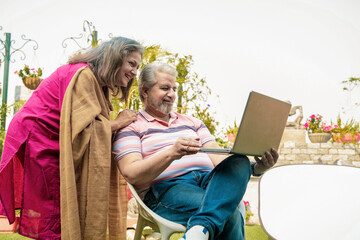 Senior Indian Couple using laptop at home garden