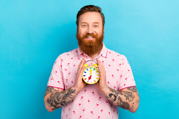Photo of funny positive man successful banker wear pink trendy clothes two hands hold alarm clock isolated on blue color background
