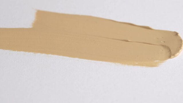 A smear of foundation cream or concealer with a brush on a white background, macro. Texture of cosmetic liquid foundation or beige cream smudge, smear, stroke. Advertising of professional cosmetics.