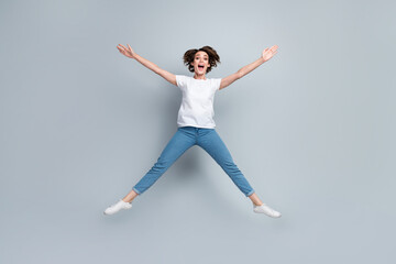 Full size photo of astonished ecstatic girl dressed white t-shirt jeans jumping like star hands up isolated on gray color background