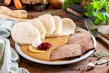 Plate of svickova na smetane, popular traditional Czech meat dish with sirloin steak prepared with vegetables, served with knedliky (dumplings), whipped cream and cranberry sauce on the table.