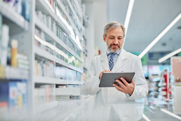 A senior male pharmacist holding a digital tablet and using it for work.