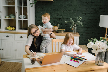 Woman working, learns on laptop computer. Mother working with kids at home. Children playing, make...