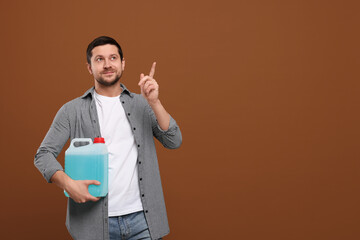 Man holding canister with blue liquid and pointing at something on brown background. Space for text