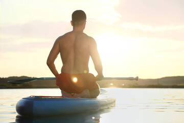 Man paddle boarding on SUP board in river at sunset, back view