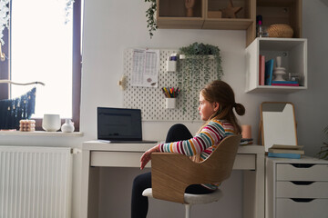 Fototapeta na wymiar Elementary age girl studying at the desk on laptop