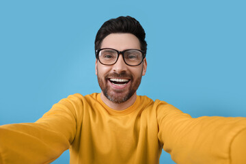 Smiling man taking selfie on light blue background