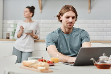 Portrait of smiling young man using laptop in kitchen during breakfast, copy space