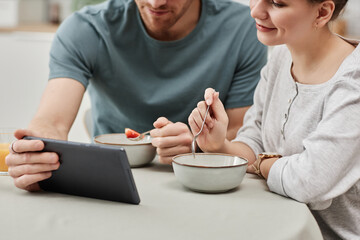 Closeup of young couple using digital tablet while enjoying breakfast in kitchen, copy space