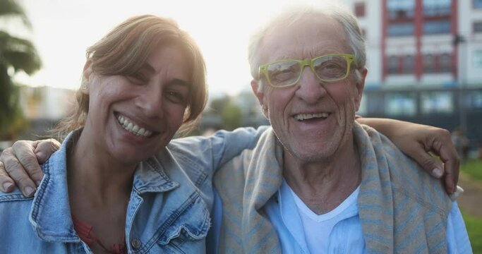 Senior man and caretaker hugging each other outdoor while smiling in front of camera 