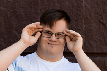 Smiling young man with down syndrome in glasses posing against stone wall background