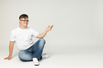 Smiling young man with down syndrome in glasses, jeans and white t-shirt posing in front of the...