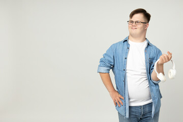Smiling young man with down syndrome in glasses with headphones in hands, place for text