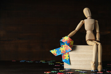 Ribbon with colorful puzzle pieces and wooden figure on dark background, place for text. World autism day concept