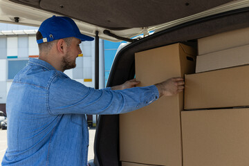 A courier with a box in his hands near a car with boxes