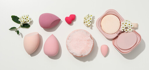 Cosmetic sponges, powder and flowers on white background, top view