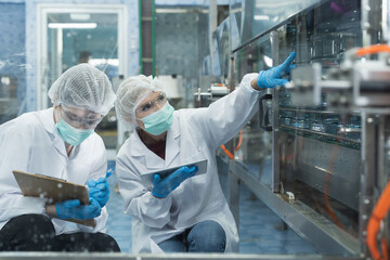 Two female worker inspecting quality of plastic water tank on conveyor belt in drinking water factory. Group of scientist using tablet working, checking bottle, gallon on conveyor production line