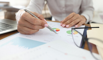 Female hand holds pen on graphs with indicators next to glasses. Small and medium business development concept