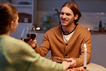 Portrait of smiling young man drinking wine with wife and enjoying romantic dinner at home