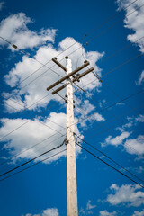 Electricity pole and power lines against the blue sky with white clouds. Summer forest landscape in Nova Scotia, Canada.