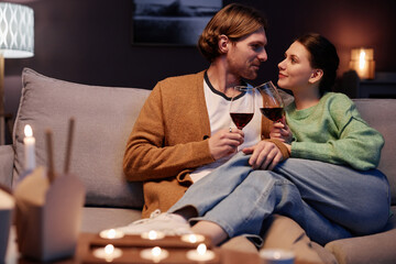 Obraz premium Portrait of young couple enjoying romantic evening at home and drinking wine cuddling on couch, copy space