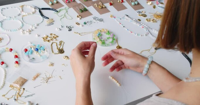 Female jewelry designer working in studio making necklace and earrings