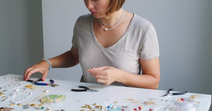 Female jewelry designer working in studio making necklace and earrings