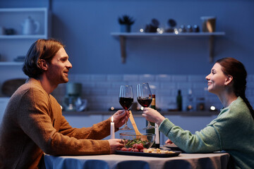 Side view portrait of young couple drinking wine while enjoying date night at home together